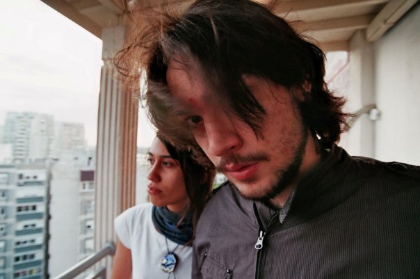 Two people pose for a photo with a cityscape in a background